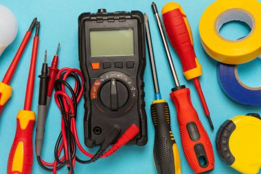 Mavi arka planda kopyalanmış elektrik teçhizatı. Üst görünüm. Elektrik aracı seti. Çoklu metre, test cihazı, tornavida, kesici, koli bandı, lamba, mezura, mezura ve kablo..