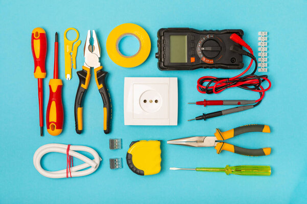 Electrician equipment on blue background with copy space.Top view.Electrician tool set.Multimeter, tester,screwdrivers,cutters,duct tape,lamps,tape measure and wires.Flet lay.