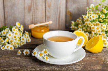 Çiçek tomurcuklu papatya çayı, kahverengi ahşap bir masada bal ve limon ve bir buket papatya çayı. Yararlı bitkisel içecekler ve doğal iyileştirici konsept. Dokunulmazlık Çayı. Kapatın. Boşluğu kopyala.