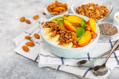 Yoğurt ve taze badem, yaban mersini, ahududu, şeftali, kivi, çilek ve muz ile dokulu mutfak masası. Boşluğu kopyala. Metin için yer.