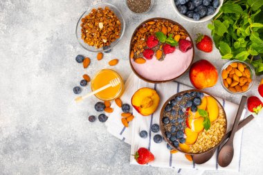 Yoğurt ve taze badem, yaban mersini, ahududu, şeftali ve çilekli granola kasesi mermer mutfak masasında. cai ve spirulina kasesi. Sağlıklı kahvaltı kavramı. Kopya alanı..