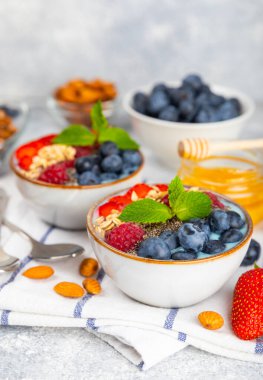 Yoğurt ve taze badem, yaban mersini, ahududu, şeftali ve çilekli granola kasesi mermer mutfak masasında. cai ve spirulina kasesi. Sağlıklı kahvaltı kavramı. Kopya alanı..