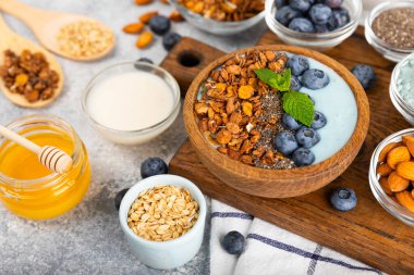 Yoğurt ve taze badem, yaban mersini, ahududu, şeftali ve çilekli granola kasesi mermer mutfak masasında. cai ve spirulina kasesi. Sağlıklı kahvaltı kavramı. Kopya alanı..