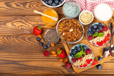 Kahverengi mutfak masasında yoğurt, taze badem, yabanmersini, ahududu, şeftali ve çilekli granola kasesi..