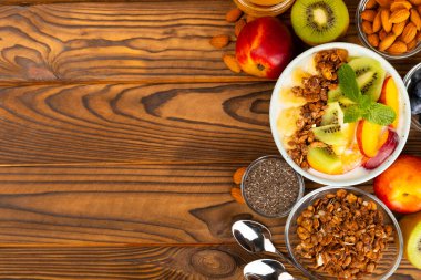 Yoğurt ve taze badem, yaban mersini, ahududu, şeftali, kivi, çilek ve muz ile dokulu mutfak masası. Boşluğu kopyala. Metin için yer.