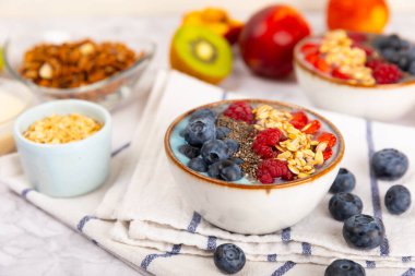 Yoğurt ve taze badem, yaban mersini, ahududu, şeftali ve çilekli granola kasesi mermer mutfak masasında. cai ve spirulina kasesi. Sağlıklı kahvaltı kavramı. Kopya alanı..