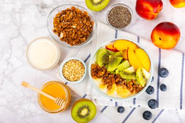 Yoğurt ve taze badem, yaban mersini, ahududu, şeftali, kivi, çilek ve muz ile dokulu mutfak masası. Boşluğu kopyala. Metin için yer.