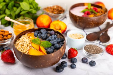 Yoğurt ve taze badem, yaban mersini, ahududu, şeftali ve çilekli granola kasesi mermer mutfak masasında. cai ve spirulina kasesi. Sağlıklı kahvaltı kavramı. Kopya alanı..