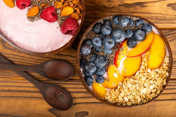 Granola bowl with yogurt and fresh almonds, blueberries, raspberries,peach and strawberries on a brown kitchen table.Acai and spirulina bowl.Healthy breakfast concept.