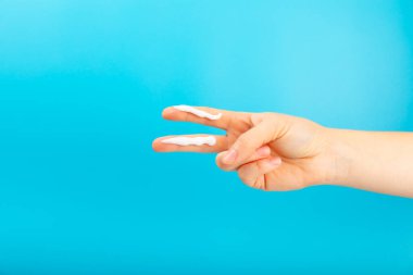 Mavi arka planda güneş kremi. SPF kremi. Yüzüne ve boynuna doğru miktarda güneş kremi süren bir kişi. Ultraviyole koruma. Yaz. Dinlenme ve tatil kavramı.