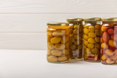 Lezzetli yeşil, siyah ve kırmızı zeytinler. Cam kavanozda zeytin turşusu. Ahşap bir arka planda. Lezzetli zeytinler. Yakın plan. Vejetaryen. Mesaj için yer. Boşluğu kopyala. Çeşitli. Farklı türde zeytin..