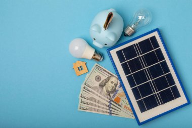 Güneş paneli, lamba, para ve doku arka planında domuz kumbarası olan düz bir kompozisyon. Tasarruf ve temiz enerji kavramı. Ekoloji ve sürdürülebilir gelişme kavramı. Teknolojiler.