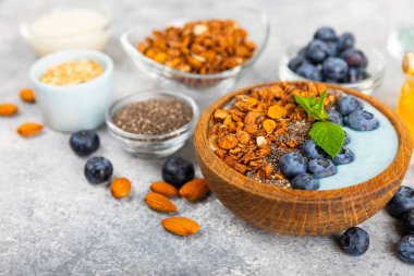 Bir kase granola yoğurt ve dokuma masasında taze böğürtlen. Yoğurt böğürtlen, acai kasesi, spirulina kasesi. Sağlıklı yemek, dengeli kahvaltı. Çilek, yabanmersini, kivi, şeftali, badem ve chia..