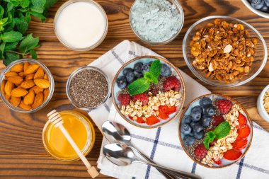 Bir kase granola yoğurt ve dokuma masasında taze böğürtlen. Yoğurt böğürtlen, acai kasesi, spirulina kasesi. Sağlıklı yemek, dengeli kahvaltı. Çilek, yabanmersini, kivi, şeftali, badem ve chia..