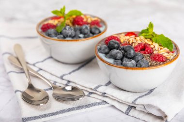 Bir kase granola yoğurt ve dokuma masasında taze böğürtlen. Yoğurt böğürtlen, acai kasesi, spirulina kasesi. Sağlıklı yemek, dengeli kahvaltı. Çilek, yabanmersini, kivi, şeftali, badem ve chia..