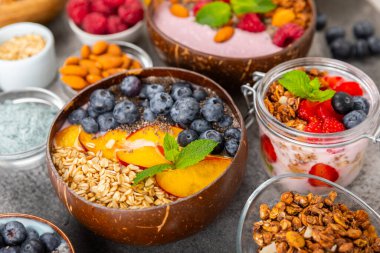 Bir kase granola yoğurt ve dokuma masasında taze böğürtlen. Yoğurt böğürtlen, acai kasesi, spirulina kasesi. Sağlıklı yemek, dengeli kahvaltı. Çilek, yabanmersini, kivi, şeftali, badem ve chia..