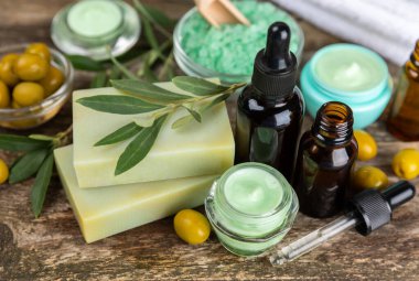 Spa zeytini. Bir kavanoz doğal zeytinyağı, temel yağlar, deniz tuzu ve kahverengi arka planda zeytin ve zeytin filizi içeren doğal el yapımı sabun içeren kompozisyon. Güzellik ve rahatlama konsepti. Düz yatıyordu
