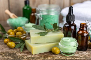 Spa zeytini. Bir kavanoz doğal zeytinyağı, temel yağlar, deniz tuzu ve kahverengi arka planda zeytin ve zeytin filizi içeren doğal el yapımı sabun içeren kompozisyon. Güzellik ve rahatlama konsepti. Düz yatıyordu
