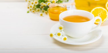 Beyaz bir masada papatya çayı. Lezzetli tonik, rahatlatıcı ve papatya çayı, papatya çiçekleri, bal ve limon. Dokunulmazlık için bitki çayı. Yakın çekim. Mesaj için yer. Boşluğu kopyala.