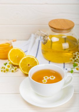 Beyaz bir masada papatya çayı. Lezzetli tonik, rahatlatıcı ve papatya çayı, papatya çiçekleri, bal ve limon. Dokunulmazlık için bitki çayı. Yakın çekim. Mesaj için yer. Boşluğu kopyala.