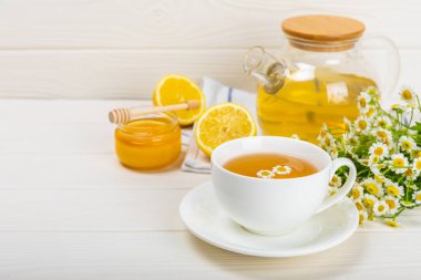 Beyaz bir masada papatya çayı. Lezzetli tonik, rahatlatıcı ve papatya çayı, papatya çiçekleri, bal ve limon. Dokunulmazlık için bitki çayı. Yakın çekim. Mesaj için yer. Boşluğu kopyala.