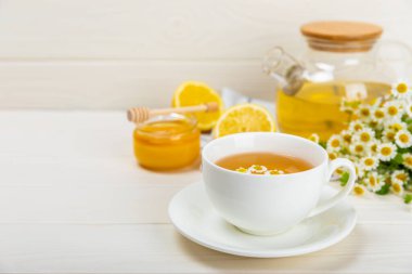 Beyaz bir masada papatya çayı. Lezzetli tonik, rahatlatıcı ve papatya çayı, papatya çiçekleri, bal ve limon. Dokunulmazlık için bitki çayı. Yakın çekim. Mesaj için yer. Boşluğu kopyala.