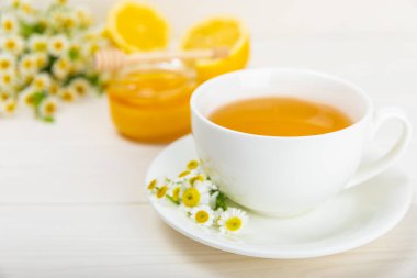 Beyaz bir masada papatya çayı. Lezzetli tonik, rahatlatıcı ve papatya çayı, papatya çiçekleri, bal ve limon. Dokunulmazlık için bitki çayı. Yakın çekim. Mesaj için yer. Boşluğu kopyala.