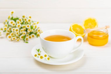 Beyaz bir masada papatya çayı. Lezzetli tonik, rahatlatıcı ve papatya çayı, papatya çiçekleri, bal ve limon. Dokunulmazlık için bitki çayı. Yakın çekim. Mesaj için yer. Boşluğu kopyala.