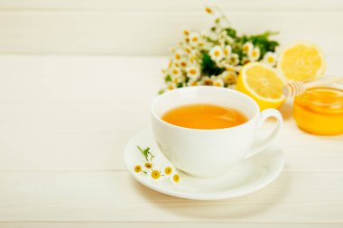 Beyaz bir masada papatya çayı. Lezzetli tonik, rahatlatıcı ve papatya çayı, papatya çiçekleri, bal ve limon. Dokunulmazlık için bitki çayı. Yakın çekim. Mesaj için yer. Boşluğu kopyala.