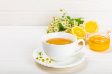 Beyaz bir masada papatya çayı. Lezzetli tonik, rahatlatıcı ve papatya çayı, papatya çiçekleri, bal ve limon. Dokunulmazlık için bitki çayı. Yakın çekim. Mesaj için yer. Boşluğu kopyala.