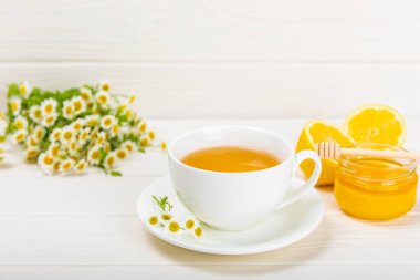 Beyaz bir masada papatya çayı. Lezzetli tonik, rahatlatıcı ve papatya çayı, papatya çiçekleri, bal ve limon. Dokunulmazlık için bitki çayı. Yakın çekim. Mesaj için yer. Boşluğu kopyala.