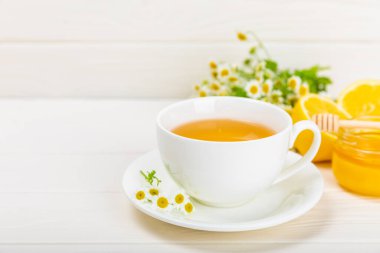 Beyaz bir masada papatya çayı. Lezzetli tonik, rahatlatıcı ve papatya çayı, papatya çiçekleri, bal ve limon. Dokunulmazlık için bitki çayı. Yakın çekim. Mesaj için yer. Boşluğu kopyala.