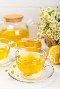 Beyaz bir masada papatya çayı. Lezzetli tonik, rahatlatıcı ve papatya çayı, papatya çiçekleri, bal ve limon. Dokunulmazlık için bitki çayı. Yakın çekim. Mesaj için yer. Boşluğu kopyala.