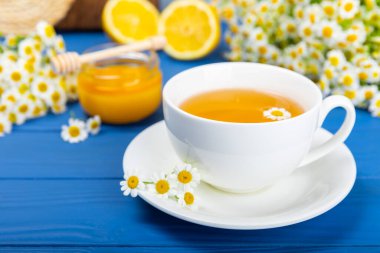 Mavi bir masada papatya çayı. Lezzetli tonik, rahatlatıcı ve papatya çayı, papatya çiçekleri, bal ve limon. Dokunulmazlık için bitki çayı. Yakın çekim. Mesaj için yer. Boşluğu kopyala.