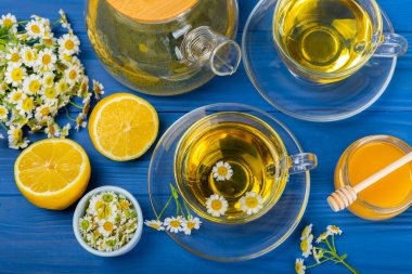 Mavi bir masada papatya çayı. Lezzetli tonik, rahatlatıcı ve papatya çayı, papatya çiçekleri, bal ve limon. Dokunulmazlık için bitki çayı. Yakın çekim. Mesaj için yer. Boşluğu kopyala.