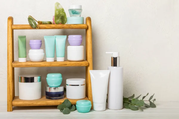Care cosmetics on the shelf in the bathroom. Cosmetic tube. Cleanser, face and body cream, face roller and gua sha, tonic. Shelf with cosmetics in the interior of the bathroom.Beauty concept.