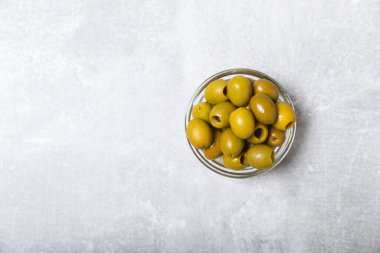 Açık mermer zemin üzerinde yeşil zeytinler. Bir kâse taze zeytin ve taze zeytin yaprakları. Vejetaryen. Zeytin meyveleri. Mesaj için yer. Boşluğu kopyala.