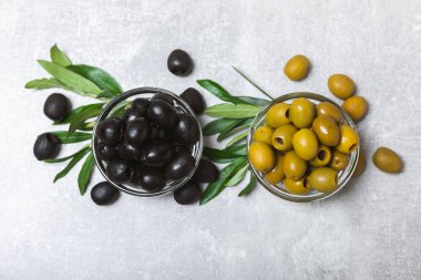 Açık mermer zemin üzerinde siyah ve yeşil zeytinler. Bir kâse taze zeytin ve taze zeytin yaprakları. Vejetaryen. Zeytin meyveleri. Mesaj için yer. Boşluğu kopyala.