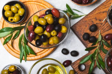 Açık mermer zemin üzerinde yeşil, kırmızı ve siyah zeytin seti. Kâselerde çeşitli zeytin ve taze zeytin yaprakları. Vejetaryen. Zeytin meyveleri. Mesaj için yer. Boşluğu kopyala.