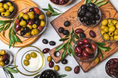 Açık mermer zemin üzerinde yeşil, kırmızı ve siyah zeytin seti. Kâselerde çeşitli zeytin ve taze zeytin yaprakları. Vejetaryen. Zeytin meyveleri. Mesaj için yer. Boşluğu kopyala.