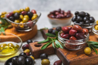 Açık mermer zemin üzerinde yeşil, kırmızı ve siyah zeytin seti. Kâselerde çeşitli zeytin ve taze zeytin yaprakları. Vejetaryen. Zeytin meyveleri. Mesaj için yer. Boşluğu kopyala.