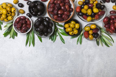 Açık mermer zemin üzerinde yeşil, kırmızı ve siyah zeytin seti. Kâselerde çeşitli zeytin ve taze zeytin yaprakları. Vejetaryen. Zeytin meyveleri. Mesaj için yer. Boşluğu kopyala.
