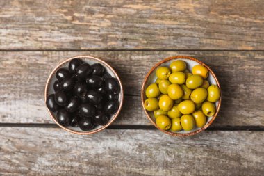 Yeşil ve siyah zeytinler, kahverengi ahşap arka planda zeytin yağı. Bir kâse taze zeytin ve taze zeytin yaprakları. Vejetaryen. Zeytin meyveleri. Mesaj için yer. Boşluğu kopyala.