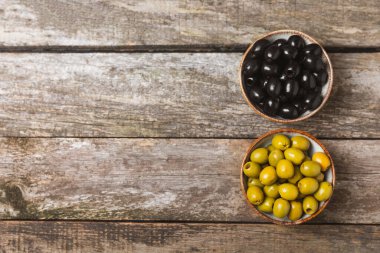 Yeşil ve siyah zeytinler, kahverengi ahşap arka planda zeytin yağı. Bir kâse taze zeytin ve taze zeytin yaprakları. Vejetaryen. Zeytin meyveleri. Mesaj için yer. Boşluğu kopyala.