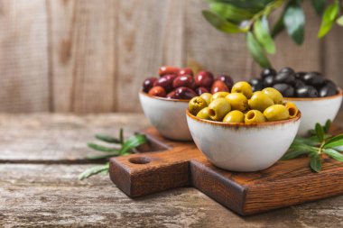 Yeşil, siyah ve kırmızı zeytinler, kahverengi ahşap arka planda zeytin yağı. Bir kâse taze zeytin ve taze zeytin yaprakları. Vejetaryen. Zeytin meyveleri. Mesaj için yer. Boşluğu kopyala.