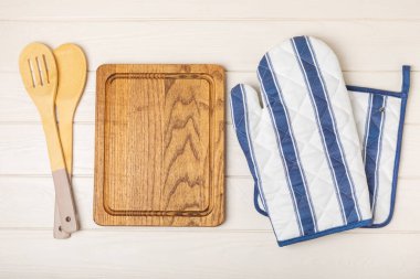 Ahşap mutfak aletleri, kesim tahtası, tutacağı ve eldiven masanın üstünde. Mutfak eldiveni ve koruyucu fırın eldivenleri masanın üstünde. Mutfak eşyaları. Mutfak aksesuarları. Yakın çekim. Üst manzara..