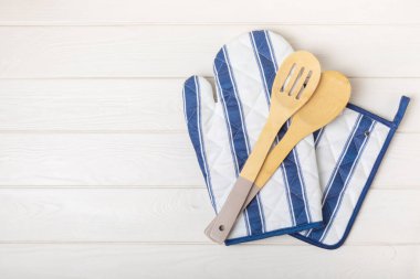 Ahşap mutfak aletleri, kesim tahtası, tutacağı ve eldiven masanın üstünde. Mutfak eldiveni ve koruyucu fırın eldivenleri masanın üstünde. Mutfak eşyaları. Mutfak aksesuarları. Yakın çekim. Üst manzara..