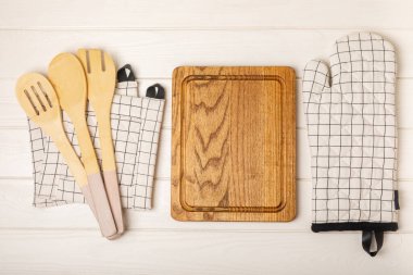 Ahşap mutfak aletleri, kesim tahtası, tutacağı ve eldiven masanın üstünde. Mutfak eldiveni ve koruyucu fırın eldivenleri masanın üstünde. Mutfak eşyaları. Mutfak aksesuarları. Yakın çekim. Üst manzara..