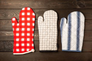 Ahşap mutfak aletleri, kesim tahtası, tutacağı ve eldiven masanın üstünde. Mutfak eldiveni ve koruyucu fırın eldivenleri masanın üstünde. Mutfak eşyaları. Mutfak aksesuarları. Yakın çekim. Üst manzara..