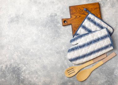 Ahşap mutfak aletleri, kesim tahtası, tutacağı ve eldiven masanın üstünde. Mutfak eldiveni ve koruyucu fırın eldivenleri masanın üstünde. Mutfak eşyaları. Mutfak aksesuarları. Yakın çekim. Üst manzara..